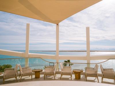 Dachterrasse mit Korbsesseln und Blick auf das blaue Meer unter bewölktem Himmel.