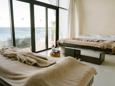 Heller Raum mit zwei Massageliegen und Meerblick durch große Fenster.