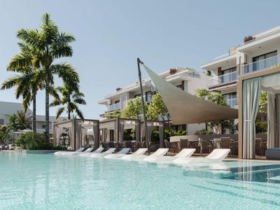 Moderner Hotelpool mit Liegestühlen, Palmen und Sonnensegeln bei klarem Himmel.