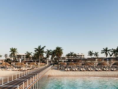 Blick auf einen Strand mit Palmen und Liegestühlen, dahinter Strandbars und Gebäude unter klarem Himmel.