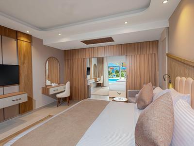 Modernes Hotelzimmer mit großem Bett, Fernseher, Schminktisch und Blick auf einen Balkon.