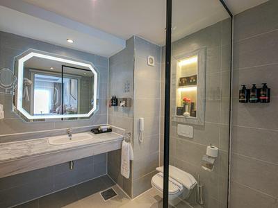 Modernes Hotelbadezimmer mit beleuchtetem Spiegel, Waschbecken und Glastür zur Dusche.