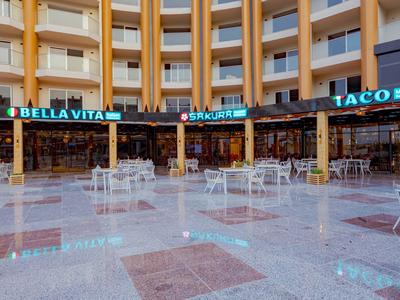 Innenhof mit Hotelbalkonen und mehreren Restaurants mit Außenbestuhlung in einem Reisekomplex.
