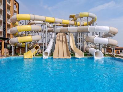 Großes Schwimmbecken mit mehreren gelben und weißen Wasserrutschen an einem Hotel.