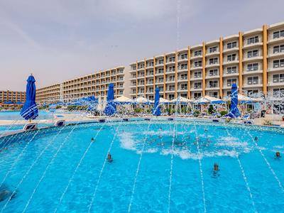 Großer Hotelpool mit Fontänen, umgeben von blauen Sonnenschirmen und mehrstöckigem Hotelgebäude.