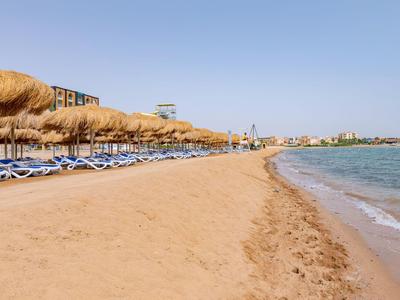 Breiter Sandstrand mit Liegestühlen und Schirmen neben ruhigem Meer und blauem Himmel.