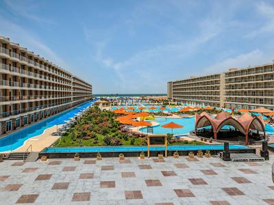 Großes Hotel mit Poollandschaft, Sonnenschirmen und Liegestühlen unter blauem Himmel.