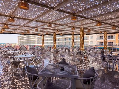 Offener Hotelterrassenbereich mit metallischen Tischen und Stühlen unter kunstvoll durchbrochener Überdachung.