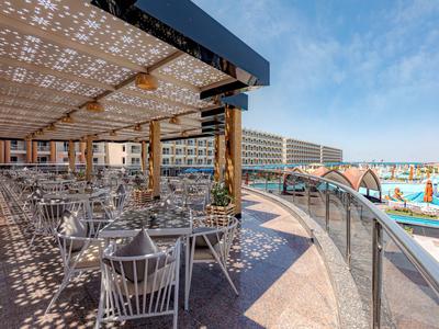 Überdachte Terrasse mit Tischen und Stühlen neben einem Pool in einem Hotel.