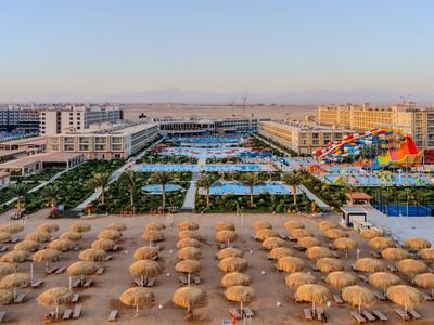 Großes Resort mit vielen Sonnenschirmen am Strand und mehreren Poolbereichen im Hintergrund.