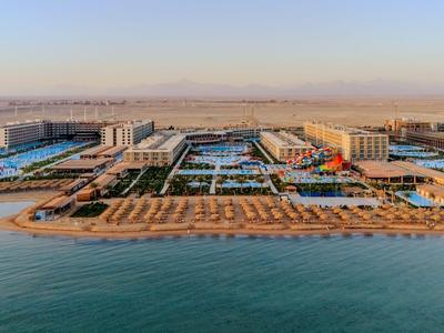 Großes Hotelresort mit Pool, Strandliegen und direktem Zugang zum Meer bei klarem Himmel.