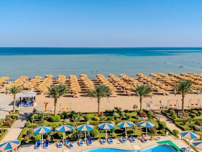 Weitläufiger Sandstrand mit Reihen von Strohdächern und blauen Sonnenschirmen am Pool.