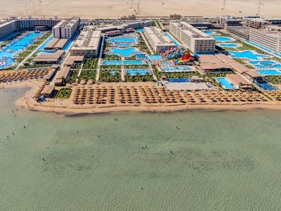 Großer Hotelkomplex mit mehreren blauen Pools und Strand am Ufer eines ruhigen Meeres.