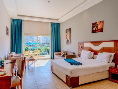 Helles Hotelzimmer mit Doppelbett, Schreibtisch und Balkon mit Blick auf Außenanlage.