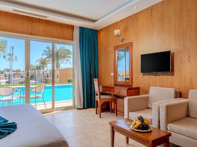 Modernes Hotelzimmer mit Sofa, Schreibtisch, TV und Blick auf den Pool durch große Fenster.