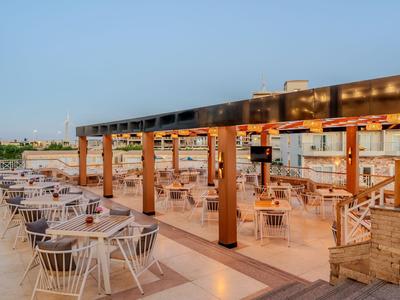 Freiluftrestaurant mit Holzbalkendach und weißen Stühlen unter klarem Himmel.