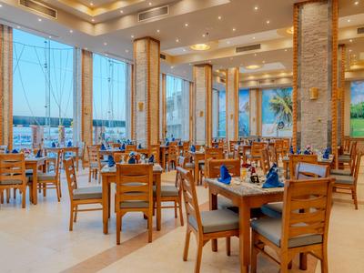 Helles Hotelrestaurant mit Holzmöbeln und großen Fenstern mit Blick auf das Wasser.