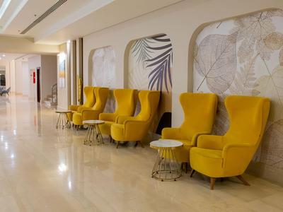 Gelbe Sessel und kleine Tische in einem hellen, modernen Hotelflur mit glänzendem Boden.