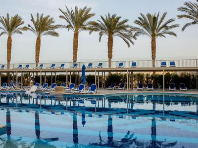 Hoteleigener Pool mit blauen Liegestühlen und Palmen im Hintergrund an einem sonnigen Tag.