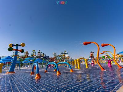 Bunter Wasserspielplatz mit vielen Rohren und spritzenden Wasserfontänen unter blauem Himmel.
