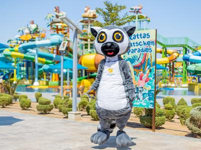 Person in Lemur-Kostüm vor Wasserrutschen in einem Wasserpark bei sonnigem Wetter.