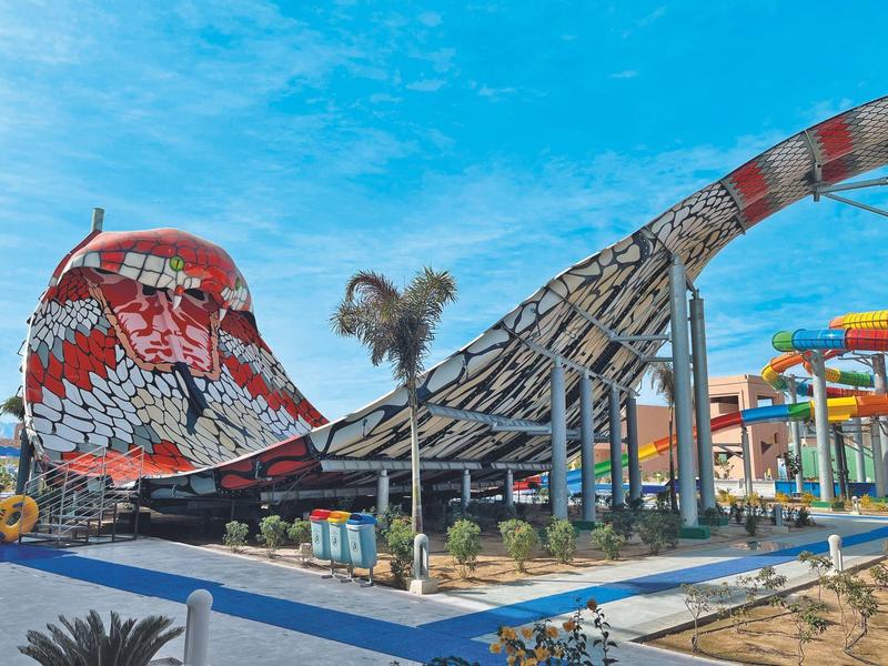 Parco acquatico moderno con scivoli, incluso uno grande rosso con motivi nero e bianco.