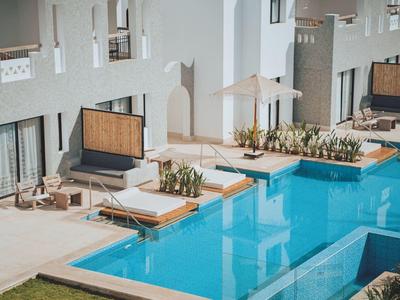 Moderner Außenbereich mit klarem Pool, Liegestühlen, Sonnenschirm und Pflanzen vor weißem Gebäude.
