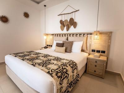 Gemütliches Schlafzimmer mit großem Bett, braunen Kissen, Deckenleuchte und Wanddekoration aus Körben.