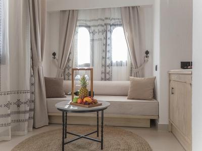 Wohnzimmer mit hellen Vorhängen, Sofa, rundem Teppich und kleinem Tisch mit Obstschale.