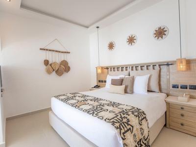 Helles Schlafzimmer mit großem Bett, Holzdeko an Wand und zwei Nachttischen mit Lampen.