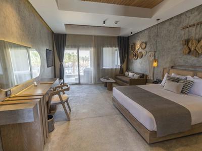 Modernes Hotelzimmer mit großem Bett, Holzmöbeln, Steinwand und Zugang zu Balkon mit Tageslicht.