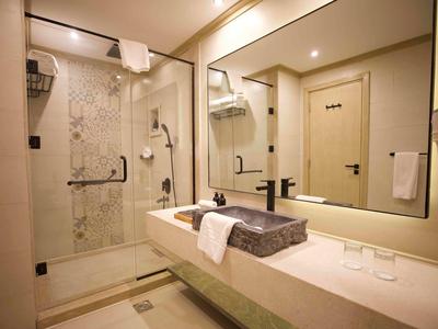 Moderner Badezimmerbereich mit Dusche, großem Spiegel und Waschbecken, warme Beleuchtung, helles Design.