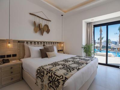 Gemütliches Schlafzimmer mit großem Bett, Holzdekor, Pflanzen und Blick auf Pool durch Glas-Schiebetür.