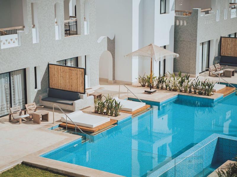 Modern hotel pool area with lounge chairs, umbrellas, and clear blue water.