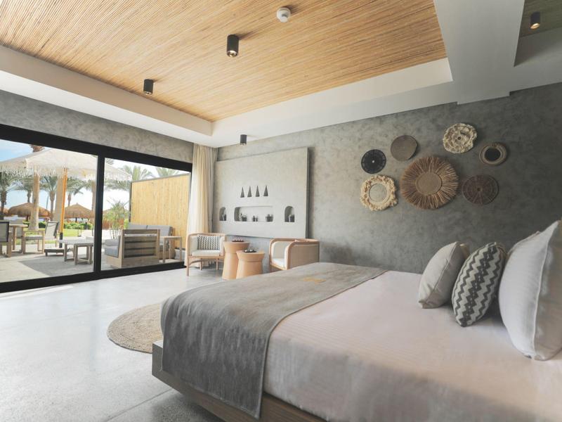 Modern hotel bedroom with large bed, sliding glass doors, and outdoor seating area.