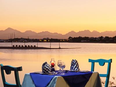 Večeře pro dva u stolu s modrým ubrusem u klidného jezera při západu slunce