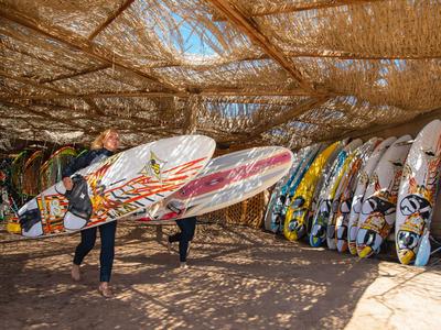 Několik malovaných surfových prken stojí pod doškovou střechou ve stínu.