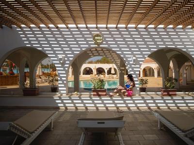 Vzory slunečního světla pokrývají oblast s lehátky a výhledem na bazén a oblouky.