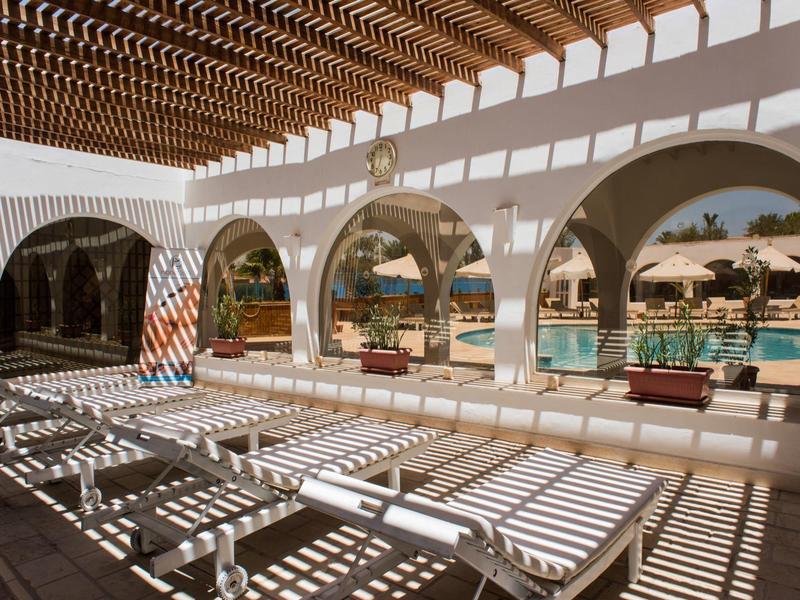 Slunečná galerie s bílými lehátky a výhledem na bazén a palmy