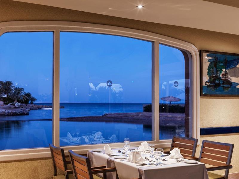 Výhled přes panoramatické okno na moře při západu slunce z restaurace.