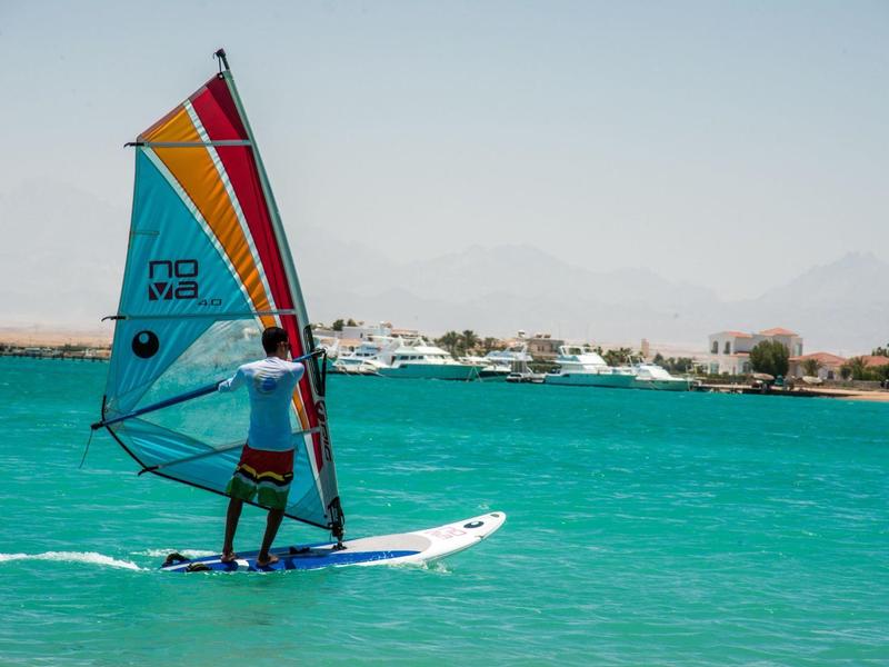 Osoba windsurfing na tyrkysové vodě s pobřežím v pozadí