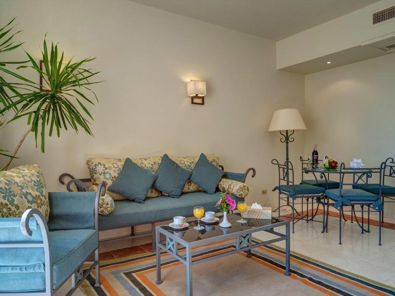 Pohodlný obývací pokoj s modrými pohovkami, skleněným konferenčním stolkem a jídelním koutem v pozadí.