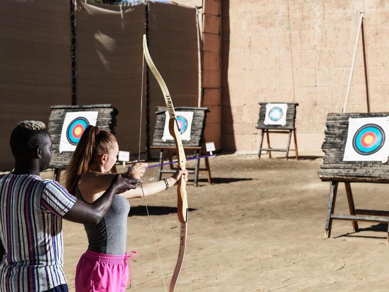 Žena dostává lekci lukostřelby od muže na venkovním prostoru s terči.