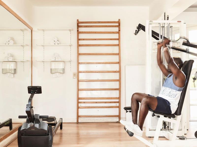 Muž cvičí na posilovacím stroji v světlé, minimalistické posilovně.