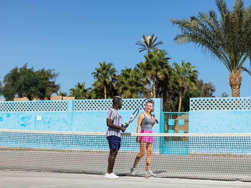 Dva lidé hrají tenis na venkovním hřišti za slunečného počasí.