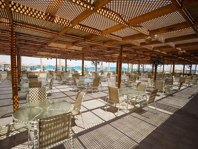 Groot overdekt terras met witte tafels en stoelen, uitzicht op zee op de achtergrond.