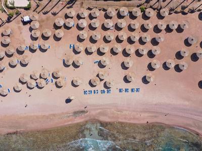 Luchtfoto van een strand met veel parasols en ligstoelen aan het water.