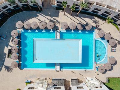 Symmetrisch rechthoekig hotelzwembad met blauw water en buitene parasols in een binnenplaats.