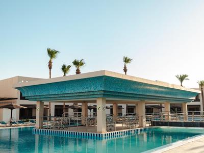Moderne hotelzwembadzondek met overdekte zithoek en palmbomen op de achtergrond.