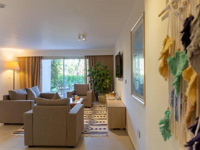 Nowoczesny salon z jasnymi sofami, dywanem i dużym oknem z widokiem na zieleń.